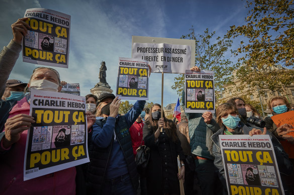 Protesters hold copies of the satirical newspaper Charlie Hebdo which read 'all that for this' during an anti-terrorism vigil at Place de La Republique for the murdered school teacher Samuel Paty who was killed in a terrorist attack in the suburbs of Paris.