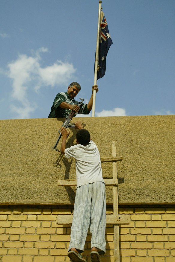 Australian embassy employee Kareem Challur holds the Australian flag and takes an AK-47 from his son Thaer, 13, on the rooftop of the embassy, which they protected in 2003. 