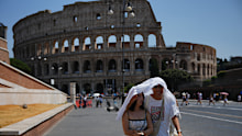 Tourists take shelter as they walk in front of the Rome’s ancient Colosseum.
