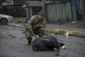 A Ukrainian serviceman uses a piece of wood to check if the body of a man dressed in civilian clothing is booby-trapped, in Bucha.
