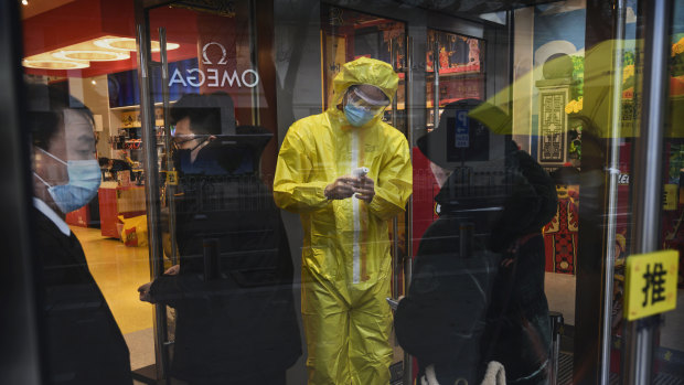 A medical worker checks customers' temperatures as they enter a store in Beijing. 