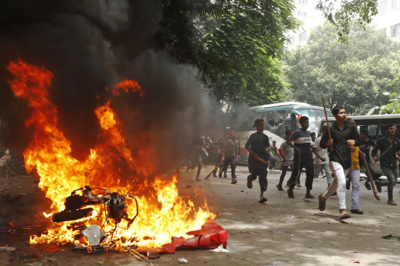 Men run past a burning vehicle set on fire by protesters during unrest in Bangladesh.