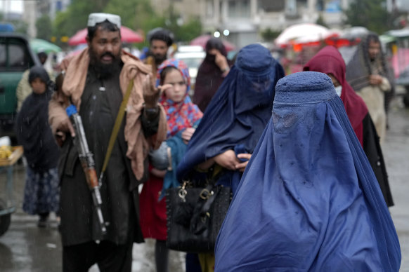 Afghan women walk through the old market as a Taliban fighter stands guard, in downtown Kabul, Afghanistan.