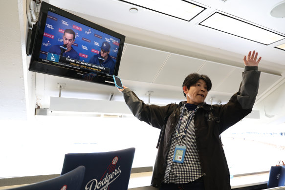 A reporter records audio from a TV at Dodger Stadium showing Shohei Ohtani’s press conference on Monday.