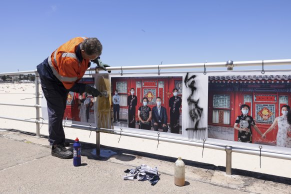 Anthony Ennis from Waverley Council cleans off graffiti on a photographic series by Horace Li, The Journey Home, exhibited at the Head On festival on Bondi Beach.