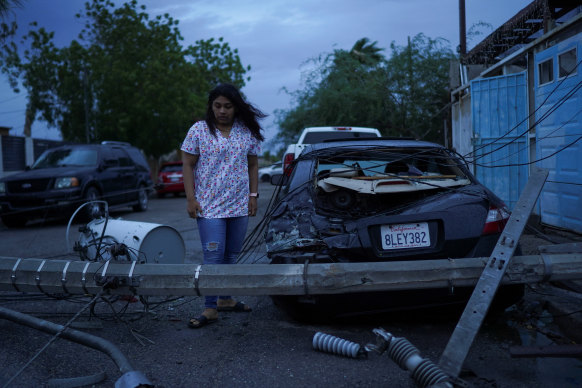 A woman observes the damage after her car was smashed by a light pole.