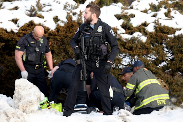 A police officer stands guard while emergency workers try to save the shot woman.