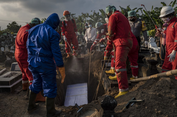Volunteers bury a COVID-19 victim in Indonesia. Some experts believe the virus will be prevalent in many parts of the world for years to come.  