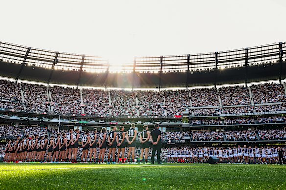 The Collingwood and Essendon teams stand for the Anzac observance at the MCG.
