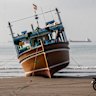 An Iranian man rides his motorcycle past a boat at Suru Beach in Bandar Abbas along the Strait of Hormuz.