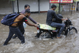 Two men help a motorcyclist navigate a flooded street after heavy rains in Ahmedabad.