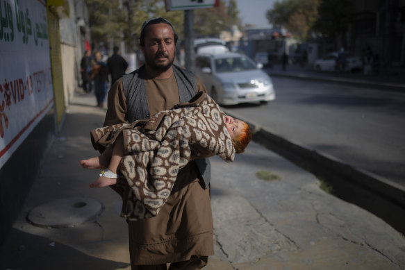 A man carries a child after the explosions at the military hospital in Kabul.