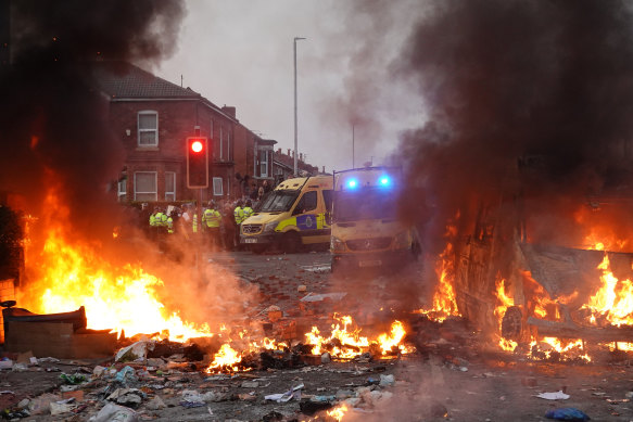 Riot police hold back protesters near a burning police vehicle after disorder broke out in Southport.