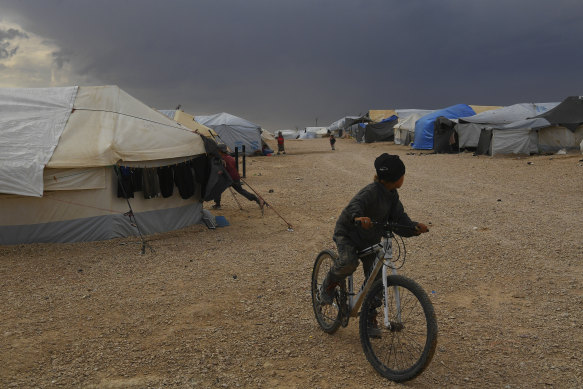 A boy on a bike looks back toward the dark clouds approaching the camp. 