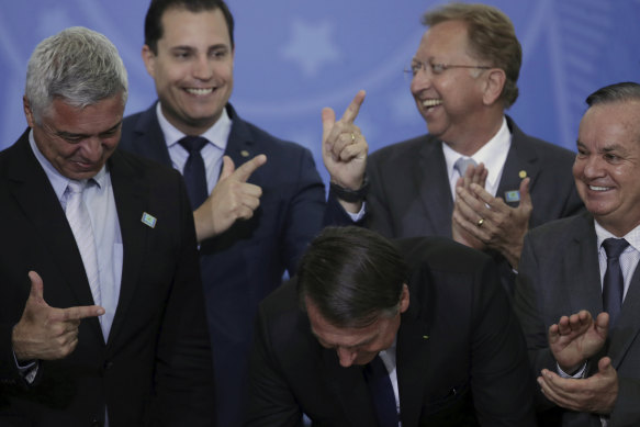 Congress members make a finger-gun hand gesture as Brazilian President Jair Bolsonaro (centre, head down) signs a second decree easing gun restrictions in Brasilia in 2019.