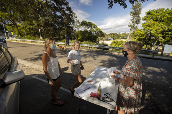 Lisa Ingram and her daughter Kira Hunter, 12, pick up RATs from Angela Clarke in Bundeena.