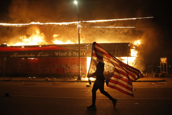 A protester carries the US flag upside down, a sign of distress, next to a burning building in Minneapolis on May 28.