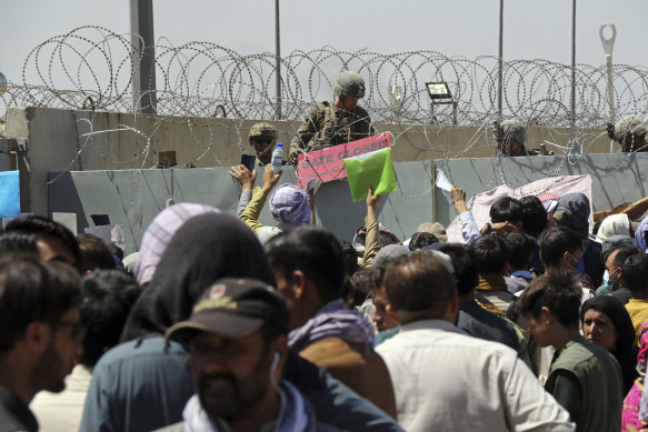 An American soldier holds a sign indicating a gate is closed as hundreds of people gather holding documents, near an evacuation control checkpoint at Kabul’s Hamid Karzai International Airport. This was the day a suicide bomber struck.