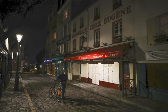 A man pushes his bicycle along a row of closed restaurants in Montmartre, Paris, during a late curfew.