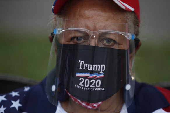 A supporter of President Donald Trump wears a mask and face shield as supporters gather for a car caravan of hundreds of vehicles, at Tropical Park in Miami.