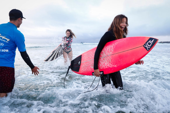 Let's Go Surfing in Byron Bay is barely surviving with the help of JobKeeper, but some people are still braving the cold including instructor Blake Whittaker with surfers Jade Stewart and Ebony Conrick.