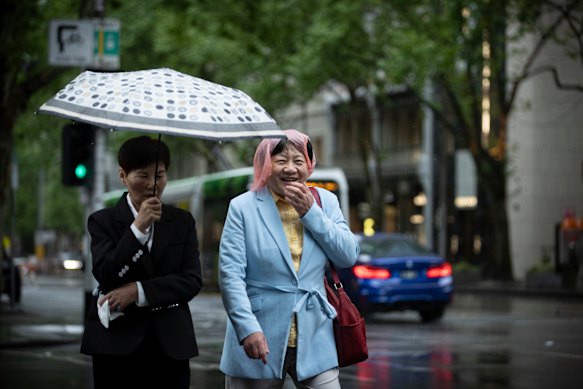 People try to shield themselves from the rain as they cross Collins Street in the Melbourne CBD.
