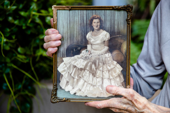 Pamela Mountfort holding a photo of her younger sister, Pat McDonald, at a Sydney university ball in a dress made by her mother. 