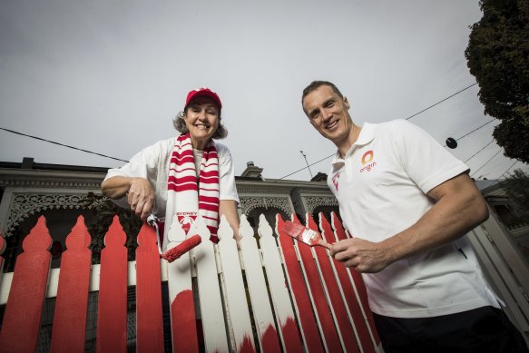 Former Swans player Ted Richards helps fan Jane Ryan paint her front fence in Sydney Swans colours.