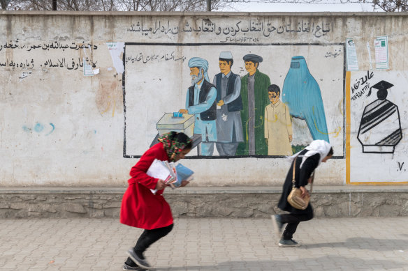 Girls head home from school in Kabul past a mural promoting voting for men and women.
