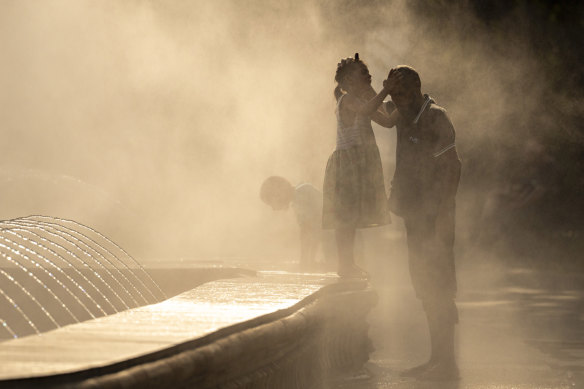 A girl and her father enjoy the mist from a public fountain in Bucharest, Romania in July.
