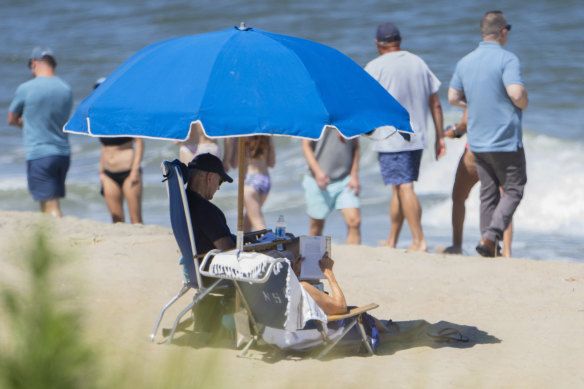 Beachgoers walk along the water as President Joe Biden and first lady Jill Biden sit underneath an umbrella in Rehoboth Beach, Delaware on Sunday.