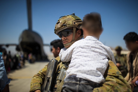 An Australian Army soldier carries an Afghan child while assisting a family aboard the RAAF C-17A Globemaster at the Hamid Karzai International Airport. 