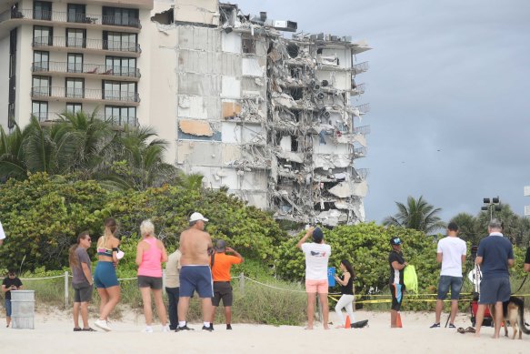 People on the beach look at the destruction to the oceanfront apartment complex.