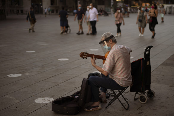 A musician wearing a face mask to prevent the spread of coronavirus plays guitar in downtown Barcelona.