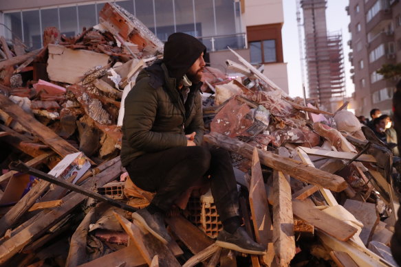 A local resident, staying outdoors for fear of aftershocks, sits ion the debris of a destroyed building as members of rescue services search for survivors in Izmir, Turkey.