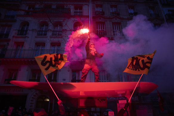 A member of the SUD stands on top of a bus shelter waving a flare as more than 400,000 people take to the streets of Paris on Thursday, as part of a nationwide strike against President Macron’s pension reform plans.
