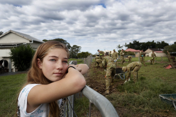Mia Harris looks on as Defence personnel help clean up her family home in Croki, near Taree, on Monday.
