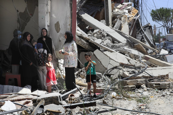 A Lebanese family stands next to a destroyed building that were hit by an Israeli airstrike, in Aita al-Shaab, a border village.