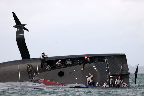 Members of the American Magic team attempt to save their yacht Patriot after it capsized in Auckland on Sunday.