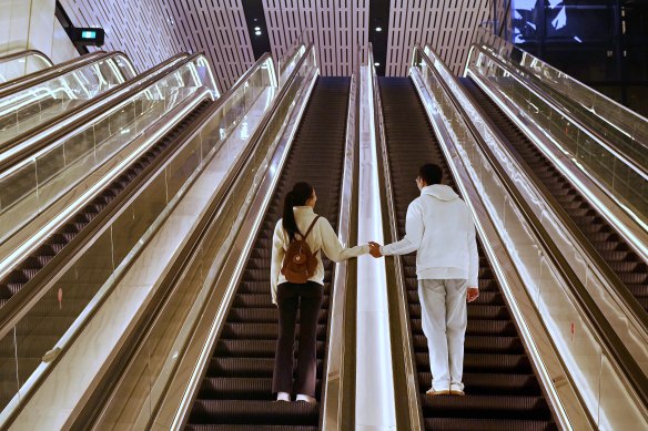 A couple hold hands as they take the escalators after disembarking from a train at the Victoria Cross Metro station in North Sydney.