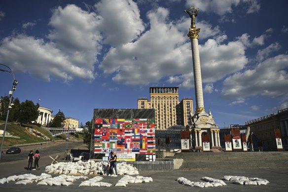 Maidan residents stand among sandbags arranged to say “Help Us” in front of a wall of flags from countries supporting Ukraine. 
