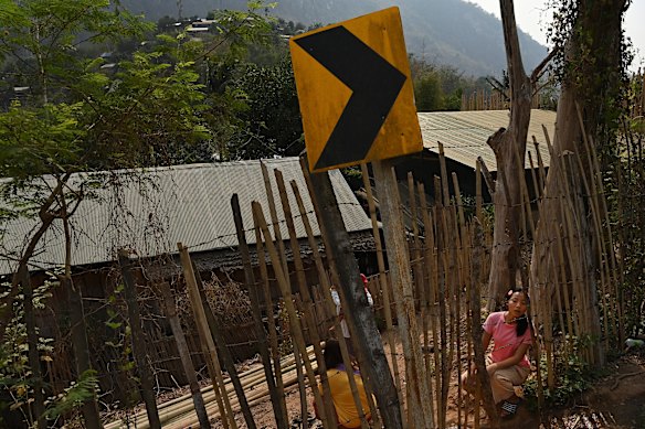 The young woman keeps watch for her ride. When it comes, her family will scamble through the  small gap in the ramshackle perimeter fence. 