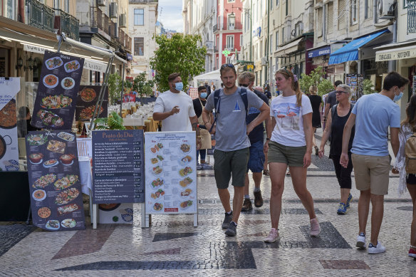 Tourists walk by a large restaurant menu and sidewalk tables in Rua das Portas de Santo Antão, Lisbon.