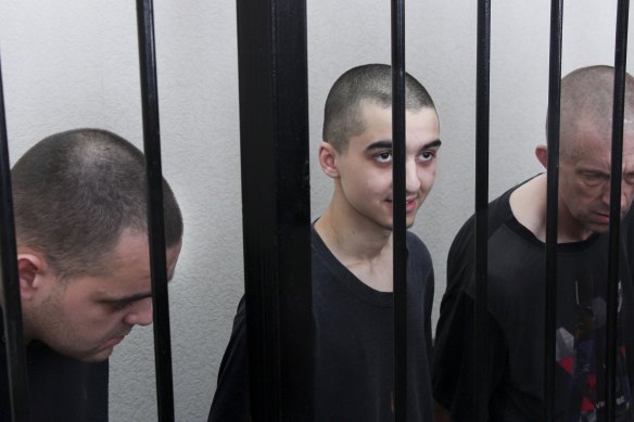 Two British citizens Aiden Aslin, left, and Shaun Pinner, right, and Moroccan Saaudun Brahim, centre, sit behind bars in a courtroom in Donetsk.