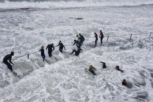 Swimmers hold the fence chains at North Narrabeen Rockpool as huge waves hammer the Sydney coast.