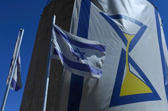 In Kibbutz Be’eri, Israeli flags fly next to a banner of an hourglass representing the fact that time is running out for the hostages in Gaza.