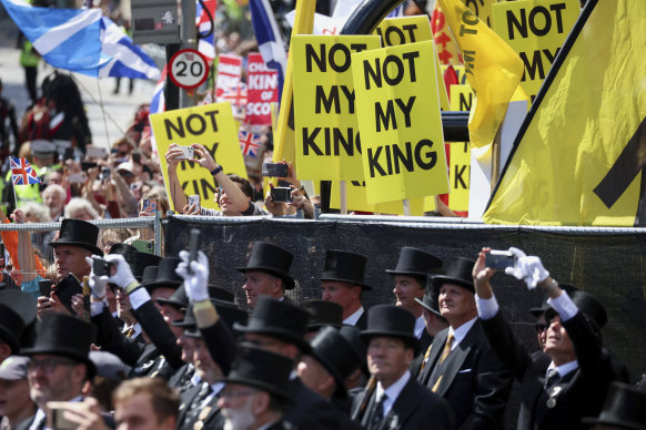 Anti-monarchy protesters hold placards near St Giles’ Cathedral as guests stand in the foreground.