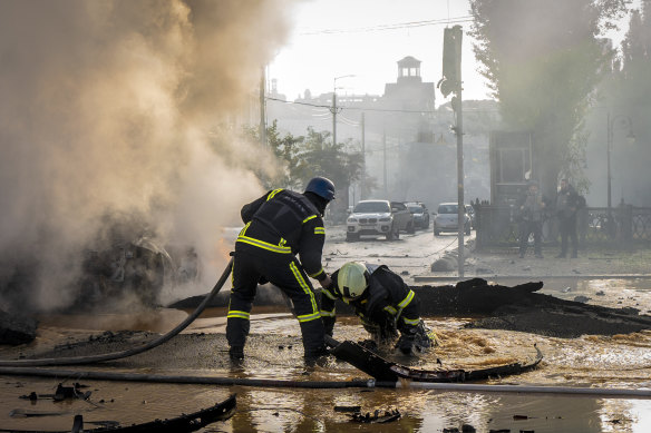 A firefighter helps his colleague  escape from a crater as they extinguish smoke from a burned car after a Russian attack in Kyiv.