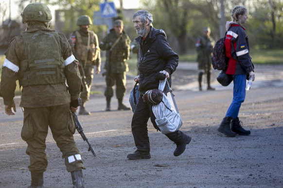 A man who left a shelter in the Metallurgical Combine Azovstal walks to a bus between servicemen of Russian Army and Donetsk People’s Republic militia in Bezimenne village in Mariupol district.