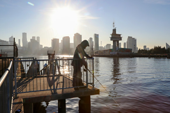 A fisherman casts his line into the Yarra River at Docklands as the sun rises over the Melbourne skyline.
